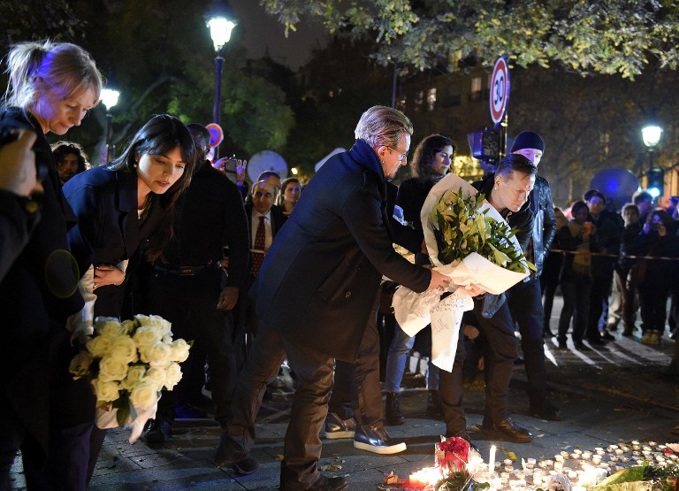 Irish band U2 lead singer Bono (C) and drummer Larry Mullen Jr (R) pay homage to attacks' victims near the Bataclan concert hall on November 14, 2015 in Paris, a day after a series of coordinated attacks in and around Paris. Islamic State jihadists claimed a series of coordinated attacks by gunmen and suicide bombers in Paris that killed at least 129 people in scenes of carnage at a concert hall, restaurants and the national stadium. U2 has canceled two sold-out concerts in Paris, including one to be broadcast live on November 14, and Foo Fighters cut short their tour after attacks that killed at least129 people. AFP PHOTO / FRANCK FIFE